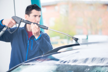 Dedicated young worker washing car manually with high-pressure hose