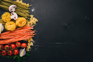 A set of pasta, noodles, spaghetti, tagliatelle, fettuccine, Farfalle. Italian cooking, fresh vegetables and spices. On a black wooden background. Top view. Copy space.