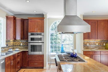 Kitchen in luxury home with stainless steel appliances, granite work surfaces, bar stools and wooden floor.