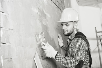 Smiling male in the helmet is plastering the wall