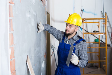 Male builder is checking the quality of the work done after the plaster wall