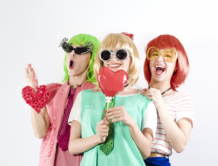 Funny young girl wearing pink wigs holding love symbols and posing for the camera on a gray background