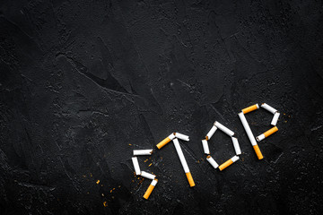 Stop smoking. Word stop lined cigarettes on black background top view copy space