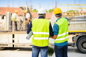 Workers in hardhat and green jacket posing on building site