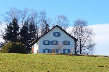 Fototapeta na wymiar Altes Bauernhaus mit blauen Fensterläden auf einem Hügel, Allgäu, Bayern