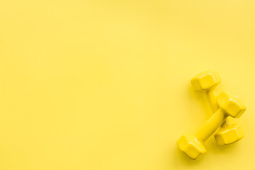 Equipment for sport exercise. Fitness background. Dumbbells, expander on pastel yellow background top view copy space