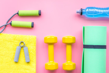 Fitness background. Equipment for gym and home. Jump rope, dumbbells, expander, mat, water on pastel pink background top view copy space