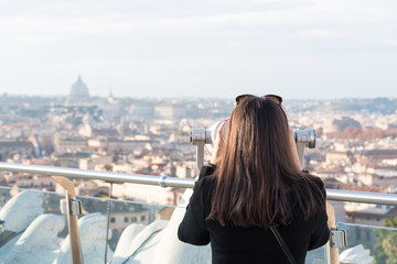 Fototapeta na wymiar Woman tourist is looking through binoculars on city Rome from a high point.
