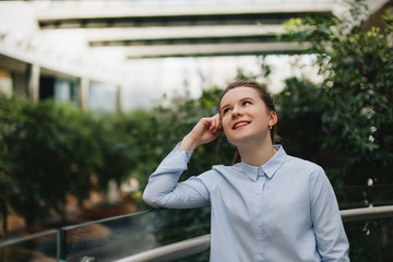 Office place with girl stand near plants. Smiling girl look at camera and around with pretty face. Office worker break, plants around.