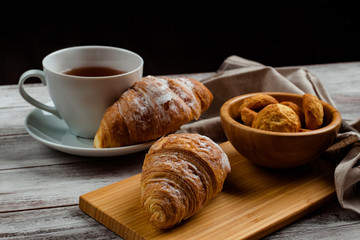 breakfast with tea and croissant on a white wooden background