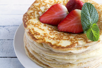 Pancakes with strawberries and mint on wooden background.