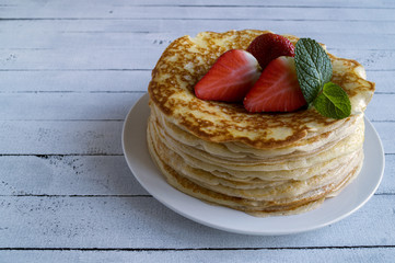 Pancakes with strawberries and mint on wooden background.