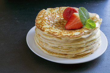 Pancakes with strawberries and mint on black background.