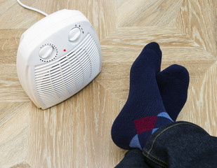 Feet in woolen winter warm socks near electric fan heater at home. Selective focus,