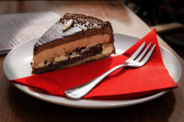 Chocolate cake on the white plate with fork and red napkin.