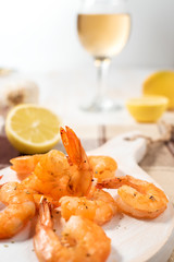 Grilled shrimps with lemon, paprika, spices and herbs on a white wooden board.