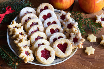 Linzer Christmas cookies arranged on a plate, with apples and spruce