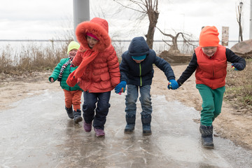 happy children in colorful clothes came on an excursion to the shore of the reservoir. Emotional children enjoy the sunny day and glide on the ice of a frozen puddle.