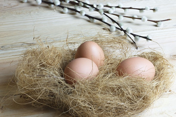 Chicken eggs in the nest on wooden background. Easter decoration.