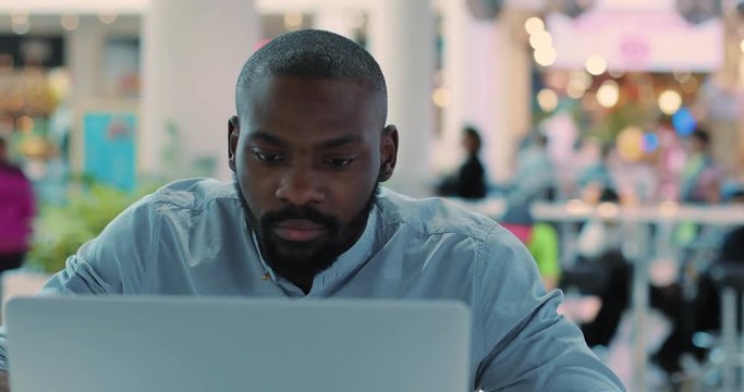 Close up face african american young man use laptop in cafe serious concentrated in mall computer web person shopping internet technology black business attractive guy sitting slow motion