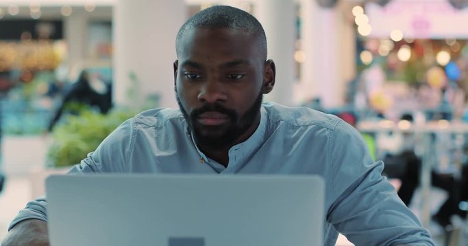 Portrait seriouse african american young man use laptop in cafe concentrated in mall computer web person shopping internet close up technology black business attractive guy sitting slow motion