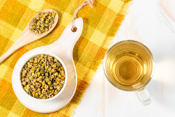 Cup of chamomile tea with dry chamomile flowers  on white wooden background.