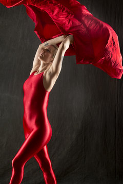 Young Woman In Red Unitard Under Red Fabric In Studio.