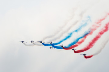 Eight aircraft at the air show demonstrate aerobatics figures and produce a multi-colored white blue red smoke