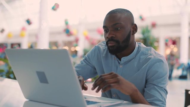 Portrait african american young man use laptop in cafe serious concentrated in mall computer web person shopping internet technology close up face black business attractive guy sitting slow motion