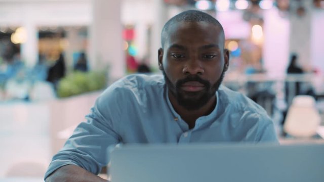 Close up face handsome african american young man use laptop smiling in cafe concentrated in mall computer person shopping internet technology black business attractive guy sitting slow motion