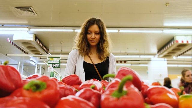 Beautiful girl chooses a red pepper in a vegetable shop in a store, 4k.