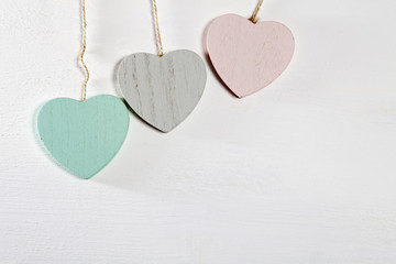 Three wooden hearts hang on a white wooden wall