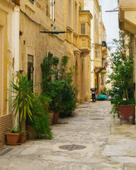 The medieval old town typical narrow street in the city Valletta on the island of Malta. Yellow balconies and classic doors and green plants near traditional style stone buildings.