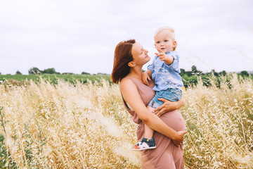Pregnant woman and son on nature. Mother waiting of a second baby.