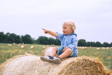 Naklejka na ściany i meble Cute toddler boy sitting on haystacks at wheat field.