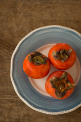 Three persimmons in a white and blue ceramic plate