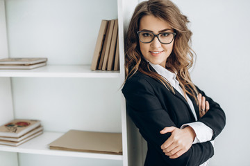 Portrait of a smiling beautiful business woman in a business suit and in glasses in a bright office