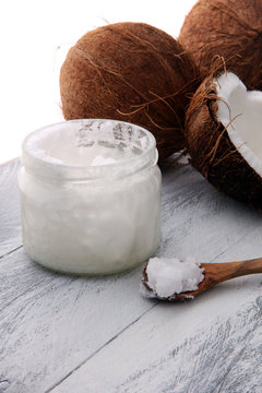 coconut and opened glass jar with fresh coconut oil on wooden background.