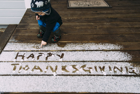 Toddler boy writing thanksgiving text with snow on wooden floor