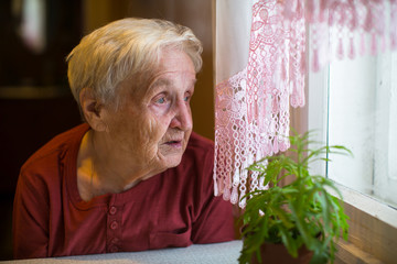Older woman with longing looks out the window.