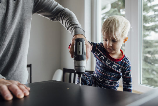 Midsection of father with son using drill on table at home