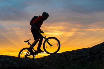 Fototapeta na wymiar Cyclist in Red Riding the Bike on Autumn Rocky Trail at Sunset. Extreme Sport and Enduro Biking Concept.