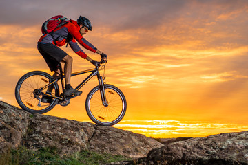 Obraz na płótnie Canvas Cyclist in Red Riding the Bike on Autumn Rocky Trail at Sunset. Extreme Sport and Enduro Biking Concept.
