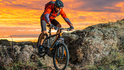 Naklejka na ściany i meble Cyclist in Red Riding the Bike on Autumn Rocky Trail at Sunset. Extreme Sport and Enduro Biking Concept.