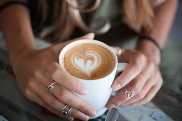 Nahaufnahme weiblicher Hände halten eine Tasse Kaffee mit Schaum in Herzform