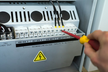 Hand of electrician with screwdriver tighten up electric terminals of transformer in electric...