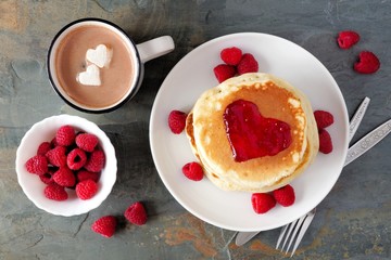 Pancakes with jam in shape of heart, hot chocolate and raspberries over a slate background. Love concept.