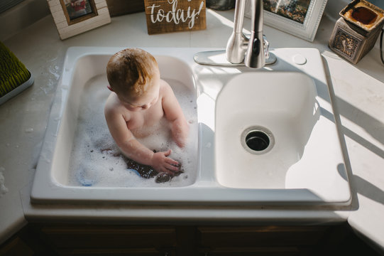 Baby boy sitting in kitchen sink at home
