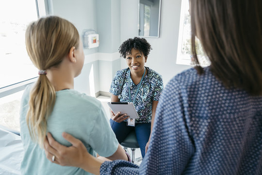 Pediatrician holding tablet computer while talking with girl sitting by mother in hospital