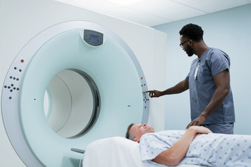 Male nurse adjusting button on MRI Scanner while patient lying in examination room